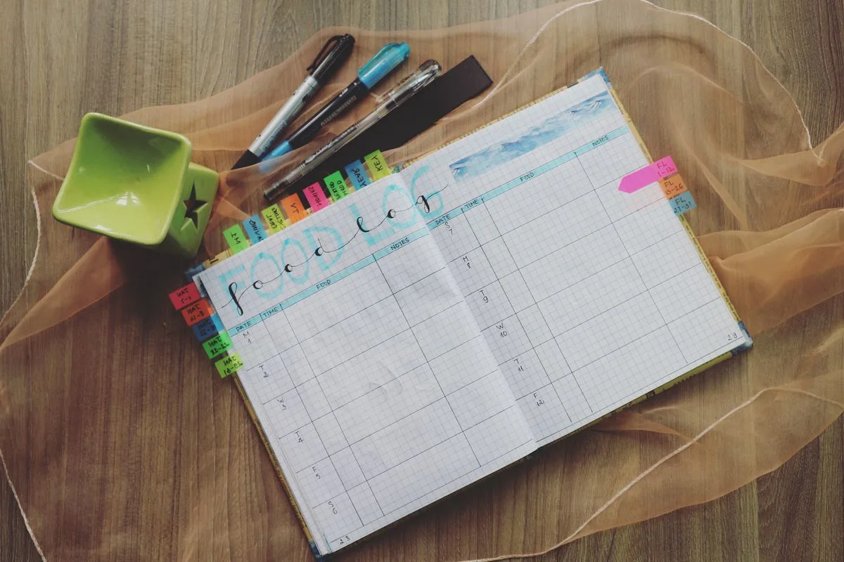 An open food log notebook with colored tabs and pens on a desk