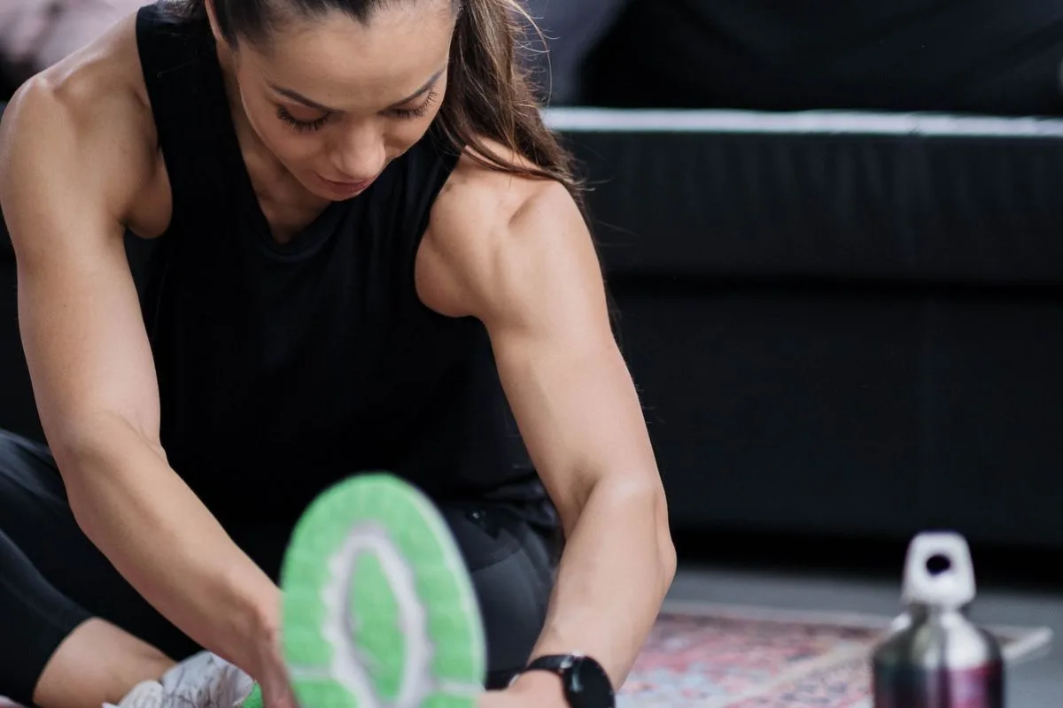 A woman tying her running shoe while stretching at home