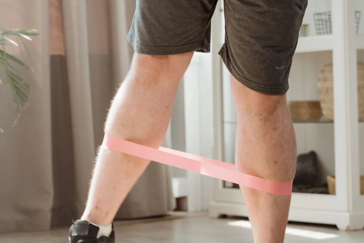 A man performing a leg exercise with a resistance band around his calves at home