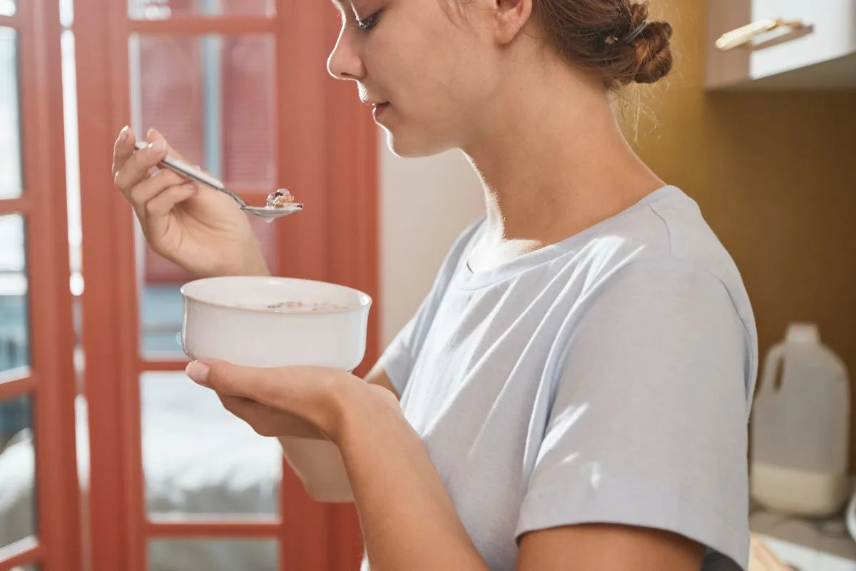 A woman savoring a bowl of breakfast slowly in a warmly lit kitchen