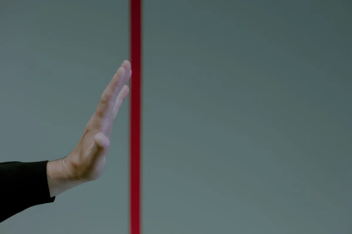 A hand raised in a stop gesture beside a vertical red line, symbolizing a boundary